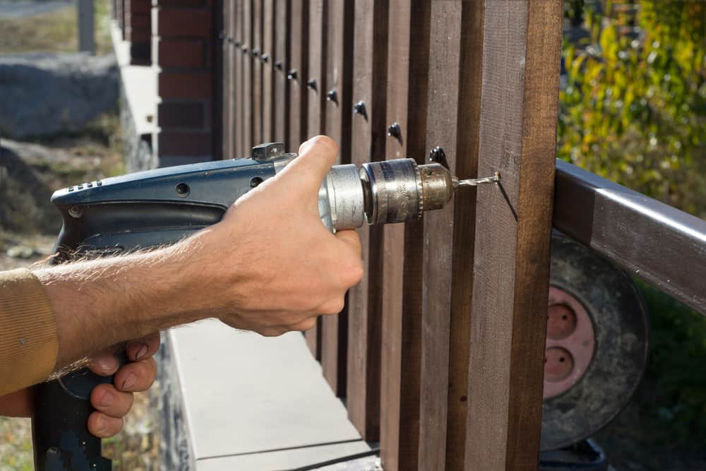 Man Hands Drilling Wooden Fence To Metal Construction.