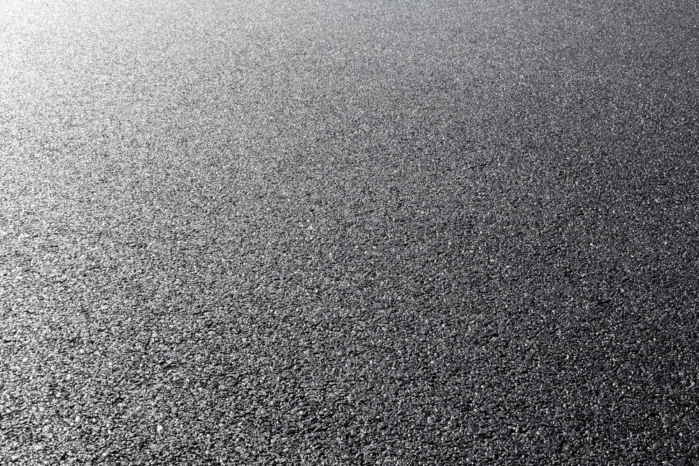 A close-up view of smooth, freshly laid asphalt pavement, glistening under bright light, showcases the expert workmanship of a masonry contractor Long Island, NY.
