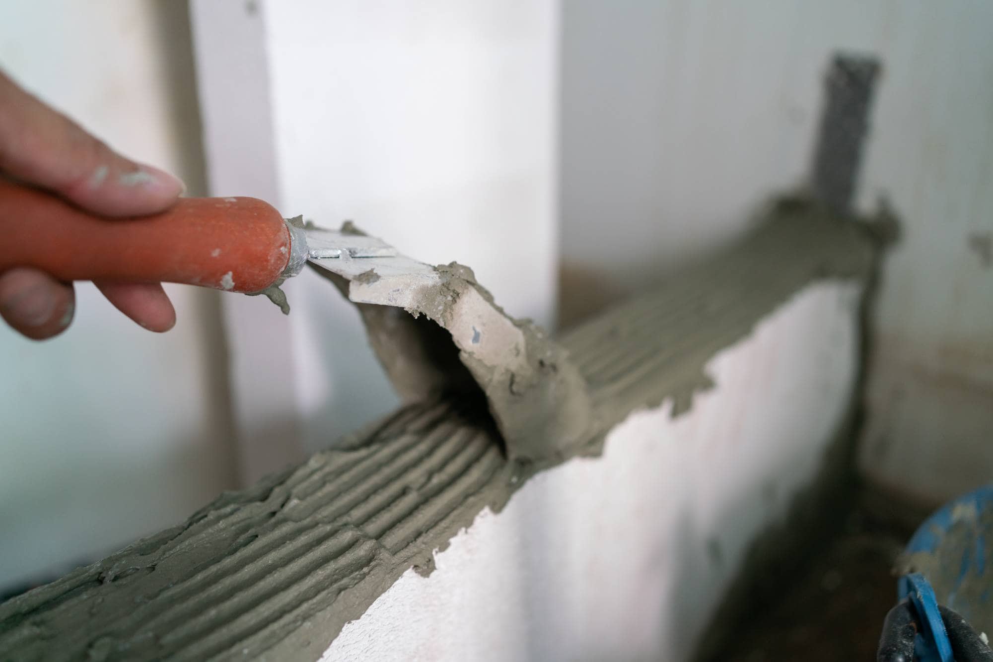 A hand holding a trowel spreads wet cement evenly along the top edge of a white brick wall under construction by a skilled masonry contractor in Long Island, NY.